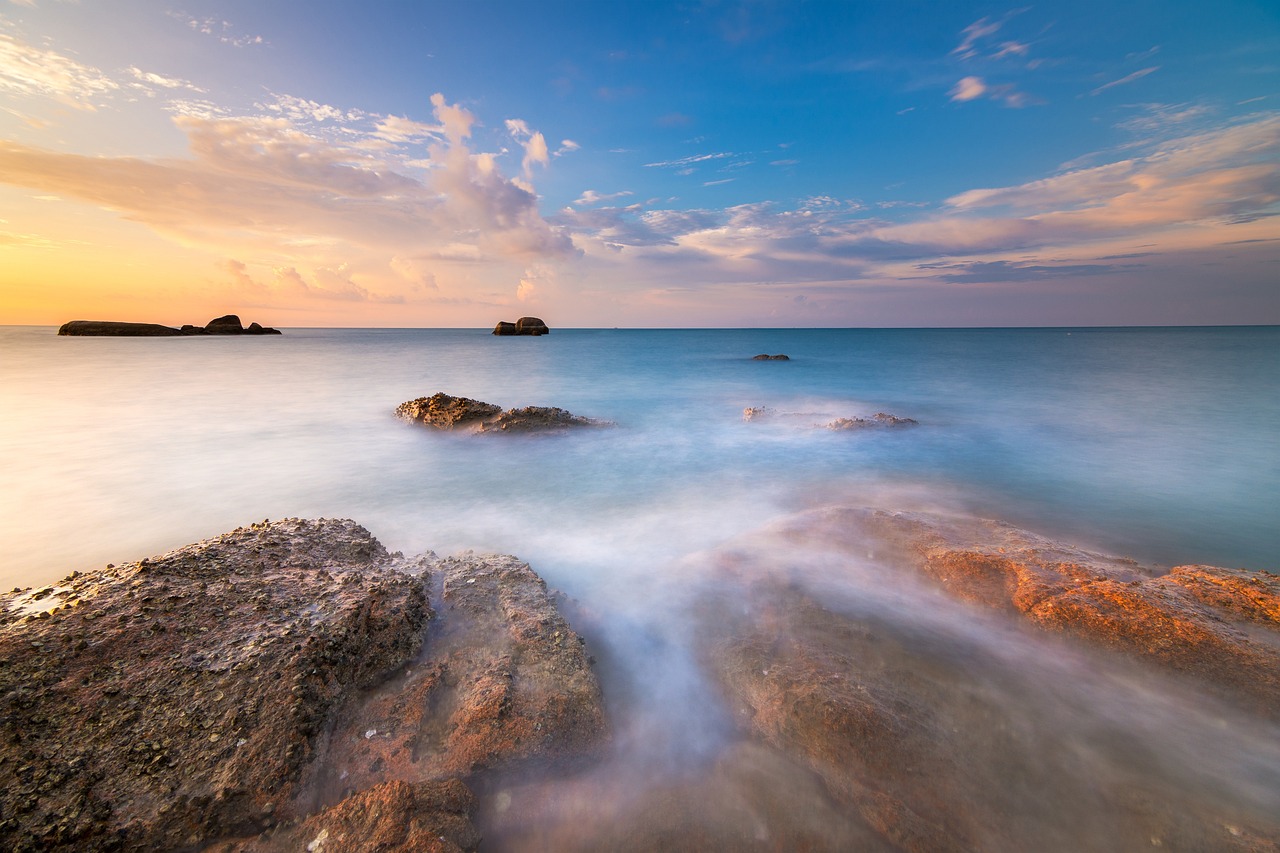 A calm seascape at sunrise with waves moving around coastal rocks